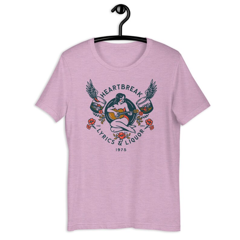 May include: Pink t-shirt with a vintage-style graphic of a woman playing a guitar with wings and glasses of liquor on either side. The text reads "Heartbreak Lyrics & Liquor 1975".