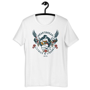 May include: White t-shirt with a vintage-style illustration of a woman playing a guitar with wings and glasses of liquor on either side. The text "Heartbreak Lyrics & Liquor 1975" is printed below the illustration.