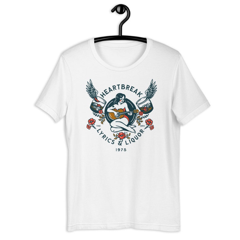 May include: White t-shirt with a vintage-style illustration of a woman playing a guitar with wings and glasses of liquor on either side. The text "Heartbreak Lyrics & Liquor 1975" is printed below the illustration.
