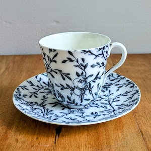 Peut inclure: Une tasse à thé et une soucoupe blanches avec un motif floral noir. La tasse a une anse et la soucoupe est ronde.