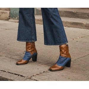 May include: Ankle boots featuring a combination of brown leather and blue denim fabric with a square toe and a block heel, worn with wide-leg dark blue denim jeans that fall to the mid-calf, creating a layered look with the boots.