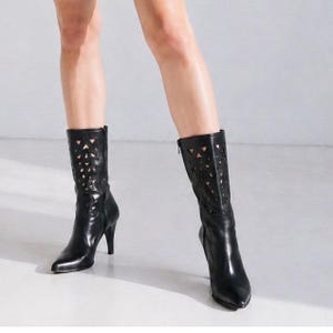 May include: A pair of black mid-calf boots featuring a pointed toe, a slim high heel, and a decorative laser-cut pattern along the upper shaft. The boots are constructed with a smooth finish and include a side zipper closure for easy access.