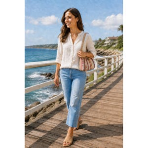 May include: A long-sleeved beige button-down shirt with a collar, light blue denim jeans with a raw hem, and a small woven shoulder bag featuring vertical stripes in shades of red, white, and brown, paired with tan slide sandals.