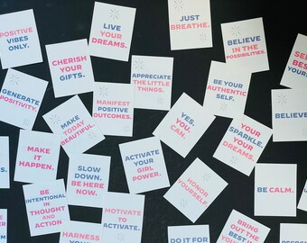 May include: A collection of motivational quotes printed on white cards with pink and blue text. The cards are arranged on a black surface. Some of the quotes include "Live Your Dreams", "Just Breathe", "Believe in the Possibilities", "Make Today Beautiful", "Be Intentional in Thought and Action", "Activate Your Girl Power", "Your Sparkle. Your Dreams.", "Be Calm", and "Bring Out the Best in You".