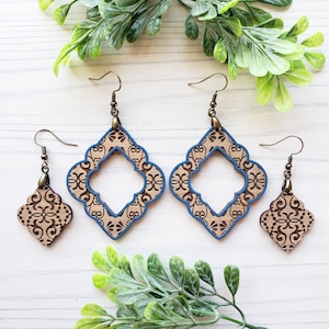 May include: A set of four wooden earrings with a blue trim. The earrings feature a geometric design with a cutout in the center. The earrings are on a white background.