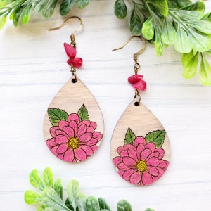 May include: A pair of wooden teardrop-shaped earrings with pink floral designs and coral-colored accents.