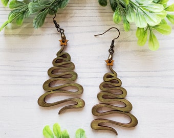 May include: A pair of wooden earrings shaped like Christmas trees. The earrings are a light brown color and have a gold star at the top.