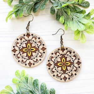 May include: A pair of wooden earrings with a yellow and brown floral design. The earrings are round and have a delicate, intricate pattern.