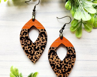 May include: A pair of orange and black leopard print dangle earrings with a teardrop shape and a cutout in the center.