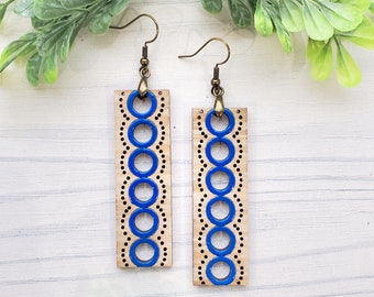 May include: A pair of wooden earrings with a blue and white geometric pattern. The earrings are rectangular in shape and have a brass hook.