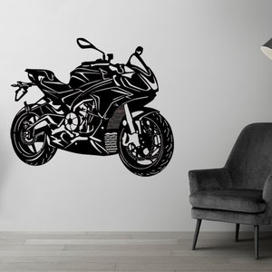 Può includere: Silhouette in bianco e nero di una motocicletta su una parete bianca. La motocicletta ha un design elegante con una grande ruota anteriore e una piccola ruota posteriore. La motocicletta è posizionata in un soggiorno con una poltrona nera e una lampada da terra.