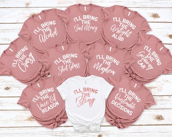May include: Nine pink t-shirts with white text that reads "I'll bring the..." followed by a different phrase on each shirt. The phrases are: "Crazy", "Alcohol", "Bail Money", "Airtight Alibi", "Shot Glass", "Mayhem", "Getaway Car", "Voice of Reason", and "Questionable Decisions". One white t-shirt with pink text that reads "I'll bring the Bling".