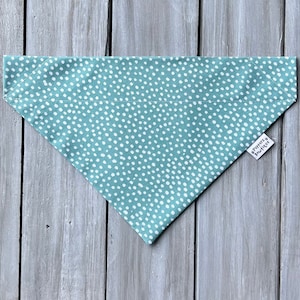 May include: A teal blue bandana with a white polka dot pattern. The bandana has a small white tag with the text "Happy & Woofin'" on it.