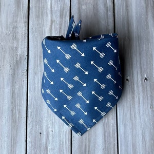 May include: A navy blue bandana with a white arrow pattern. The bandana is folded and tied in a knot.