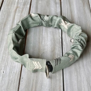 May include: A green fabric dog collar with a white and black arrow pattern. The collar has a silver D-ring.