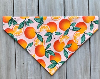 May include: A pink bandana with a pattern of orange slices and white flowers. The bandana is triangular in shape and has a white background.