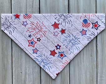 May include: A white bandana with a red, white, and blue fireworks and star pattern. The bandana is folded into a triangle shape.