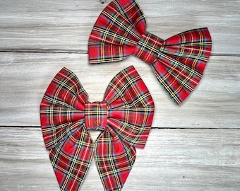 May include: Two red and green plaid fabric hair bows. The bows are tied in a classic bow shape and have a pointed end.