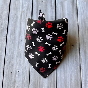 Op de afbeelding: Zwarte bandana met een wit en rood poot- en botpatroon.