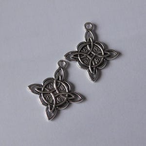 Könnte beinhalten: Zwei silberfarbene keltische Knotenanhänger. Jeder Anhänger hat ein vierzackiges Design mit komplizierten, ineinander verschlungenen Mustern und einer kleinen Schlaufe oben zum Befestigen an einer Kette oder einem Band. Geeignet für die Schmuckherstellung.