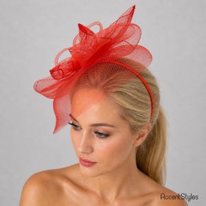 May include: A vibrant red headpiece with a floral design. The headpiece features a mesh veil and is attached to a thin red headband. The image is set against a neutral background. The text "AccentStyles" is in the bottom right corner.