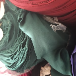 May include: Close-up of a stack of fabric rolls in various colors, including red, green, and pink. The fabric is folded and rolled, and the edges are visible. The fabric appears to be a soft, smooth material.