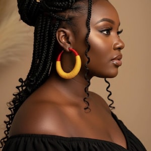 Peut inclure: Profil d'une personne portant de grandes boucles d'oreilles créoles rouges et jaunes. La personne a des cheveux noirs tressés avec des accessoires dorés et porte un haut noir à épaules dénudées.