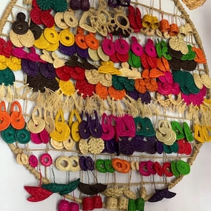 May include: A large circular woven display rack holding a wide variety of colorful raffia earrings. The collection features numerous shapes including circles, triangles, and tassels in vibrant shades of red, yellow, green, purple, and orange.