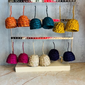 Peut inclure: Présentation de boucles d'oreilles faites à la main de différentes couleurs : orange, sarcelle, jaune, rose, beige et marine. Les boucles d'oreilles en forme de cloche sont tissées et suspendues à un présentoir argenté.