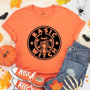 May include: Orange t-shirt with a black graphic of a witch wearing a hat and the text "BASIC WITCH" in a circle.