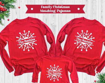 May include: Red long-sleeved shirts with a white snowflake design and the text "The Smiths" printed on them. Family Christmas matching pajamas.