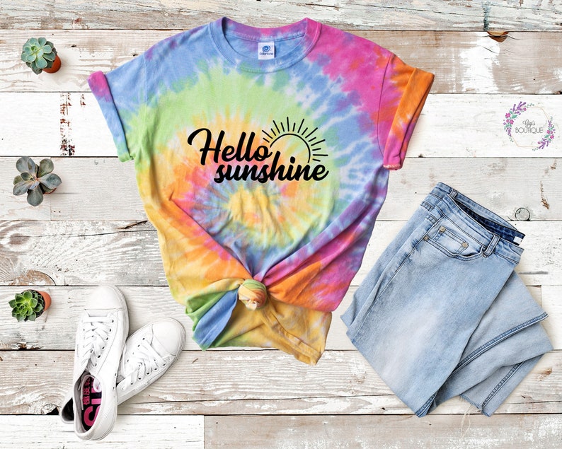 May include: A tie-dye t-shirt with the text "Hello sunshine" in black lettering. The shirt is a rainbow of colors, including pink, orange, yellow, green, and blue.