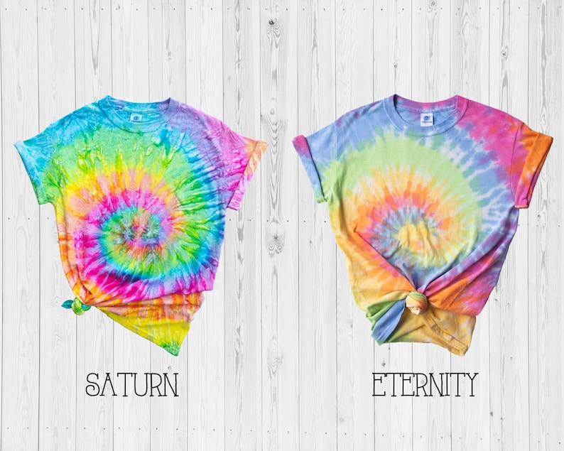 May include: Two tie-dye t-shirts with a rainbow swirl pattern. The shirt on the left is labeled "SATURN" and the shirt on the right is labeled "ETERNITY".