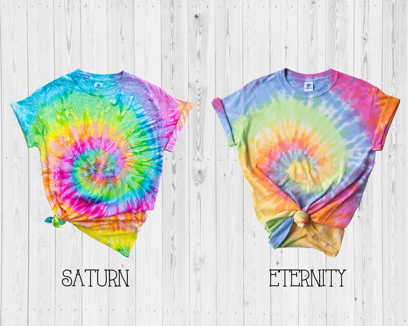May include: Two tie-dye t-shirts with a rainbow swirl pattern. The shirt on the left is labeled "SATURN" and the shirt on the right is labeled "ETERNITY".