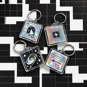 Könnte beinhalten: Vier quadratische holografische Schlüsselanhänger mit Pixel-Art-Motiven. Einer zeigt ein Computerfenster mit Cursor, einer einen Gittertunnel mit Stern, einer eine Spiralgalaxie und der letzte ein Warnfenster mit dem Text WARNING und OK.