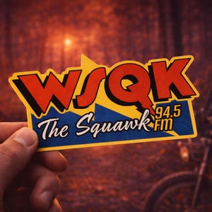 Puede incluir: Una pegatina con el texto "WSQK The Squawk FM 94.5" en rojo y azul. La pegatina tiene un fondo amarillo y azul. La pegatina está sujeta en una mano.