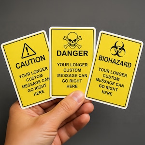 Op de afbeelding: Drie rechthoekige gele stickers met zwarte randen en tekst. De linker sticker bevat een waarschuwingsdriehoek en het woord CAUTION. De middelste sticker toont een schedel met gekruiste beenderen en DANGER. De rechter sticker toont een biohazard-symbool en BIOHAZARD. Elke sticker bevat aangepaste tekst.