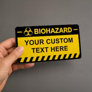 Pode incluir: Uma placa retangular com uma seção superior preta contendo o símbolo amarelo de risco biológico e a palavra BIOHAZARD. A seção central amarela maior exibe o texto YOUR CUSTOM TEXT HERE em preto, com uma borda listrada preta e amarela.