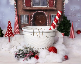 May include: A white ceramic mug with a red and white striped candy cane sticking out of it. The mug is surrounded by white cotton balls, a small green tree, a red and white striped tree, and a red ornament. The background is a blue and white winter scene with a gingerbread house.