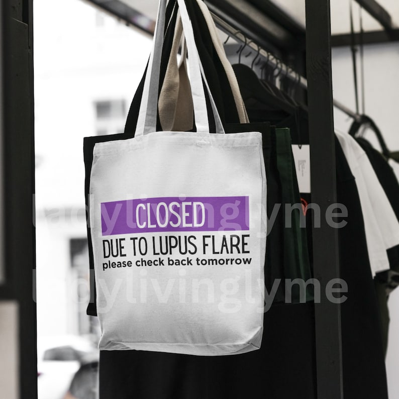 May include: White tote bag with purple text that reads "CLOSED DUE TO LUPUS FLARE please check back tomorrow".