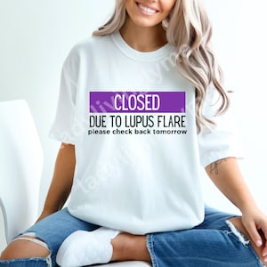 May include: White t-shirt with a purple banner that says "CLOSED DUE TO LUPUS FLARE please check back tomorrow".