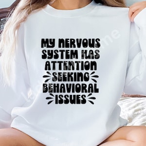 May include: White sweatshirt with black text that reads "My nervous system has attention seeking behavioral issues".