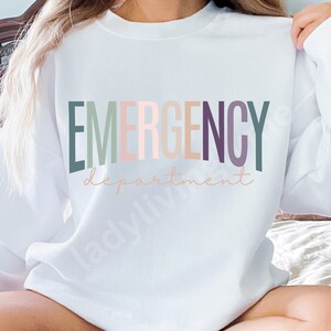 May include: White sweatshirt with the text "EMERGENCY department" in rainbow colors.