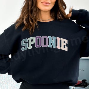 May include: Black sweatshirt with the word "SPOONIE" in colorful block letters.