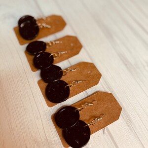 Puede incluir: Cuatro pares de pendientes circulares negros con ganchos plateados, presentados en cartulina marr&oacute;n.