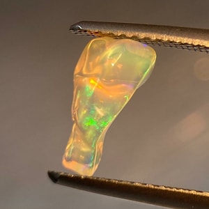 May include: A teardrop-shaped opal gemstone with a translucent, milky white body and iridescent flashes of green, yellow, and orange.
