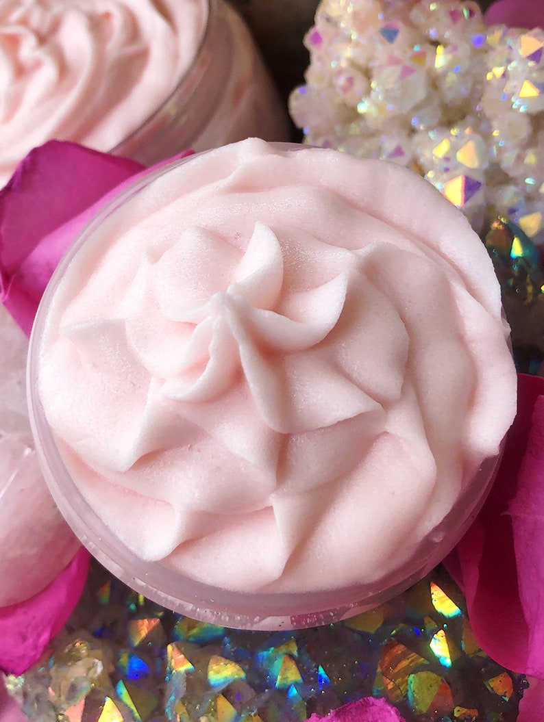 May include: Close-up of a pink whipped body butter in a clear jar. The butter is swirled and has a smooth, creamy texture.