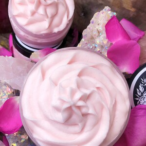 May include: Two containers of pink whipped body butter, one on top of the other, surrounded by pink rose petals and iridescent crystals.