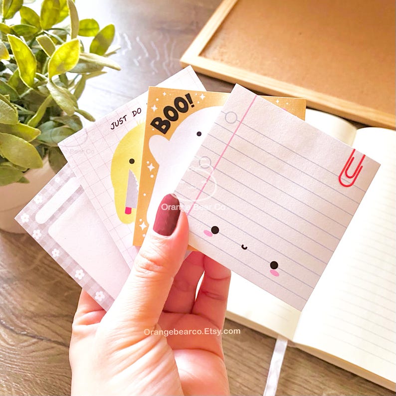 May include: A set of four colorful sticky notes with cute illustrations. The notes feature a ghost with the text "BOO!" a yellow character with the text "JUST DO", a lined note with a cute face, and a note with a gray and white checkered pattern.