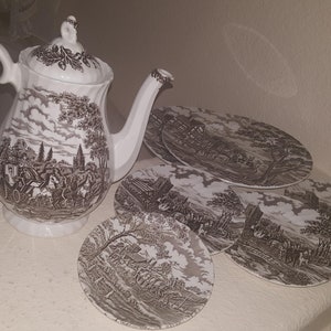 Può includere: Un set da tè marrone e bianco con una teiera e quattro piattini. La teiera ha un design floreale e i piattini hanno una scena di paesaggio marrone e bianco.